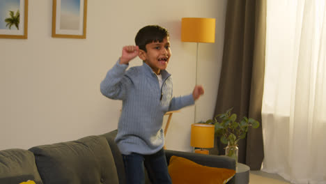 Disruptive-Young-Boy-Behaving-Badly-At-Home-Jumping-On-Sofa-Lounge